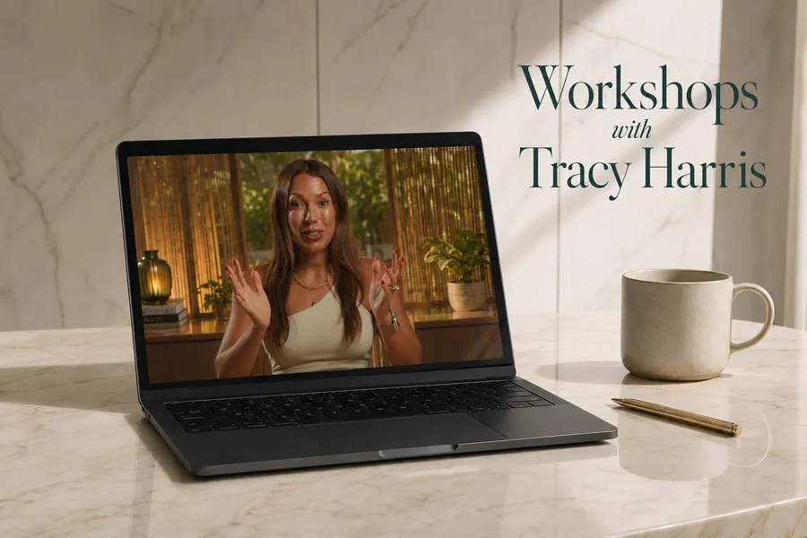 A laptop on cream marble showing Tracy Harris mid-workshop, with a sage ceramic mug and brass pen